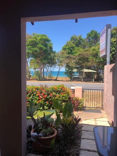 an open door with a view of the beach and flowers at Pandanus Holiday Apartments in Mission Beach