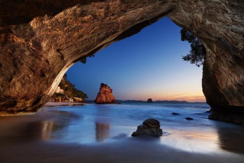 a cave on a beach with a rock in the water at Tairua Shores Motel in Tairua