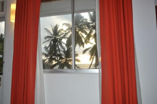 an open window with red curtains and palm trees at Star Beach Guest House in Negombo