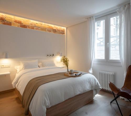 a white bedroom with a large bed and a chair at PREMIUM LOCATION! Gran Vía & FREE Parking in Bilbao