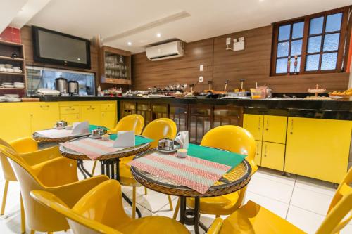 a restaurant with yellow tables and chairs and a kitchen at Hotel Gogó da Ema in Maceió