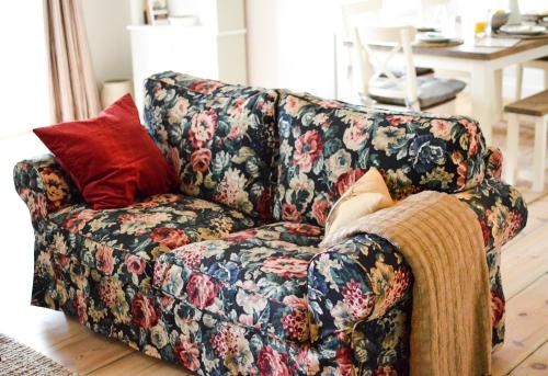 a living room with a floral couch with a red pillow at Mill Green Cottage, On site Pools & Spa access in Somerford Keynes