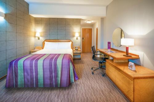 a hotel room with a bed and a desk and a mirror at Copthorne Hotel Plymouth in Plymouth