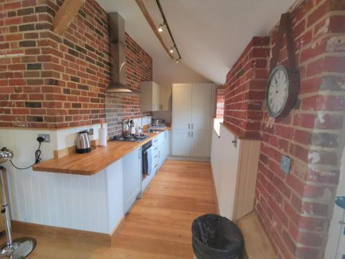 a kitchen with a brick wall and a clock on a wall at Blashford Manor Farmhouse Holiday Cottage - The Shire Cottage in Ellingham