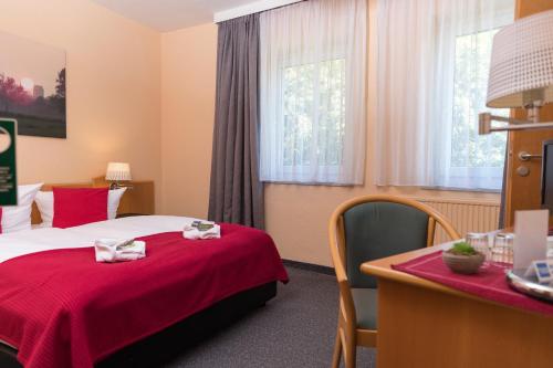 um quarto de hotel com uma cama com um cobertor vermelho em Hotel am Tierpark em Güstrow