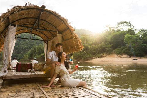 a man and a woman sitting on a dock in the water at River Kwai Jungle Rafts in Sai Yok