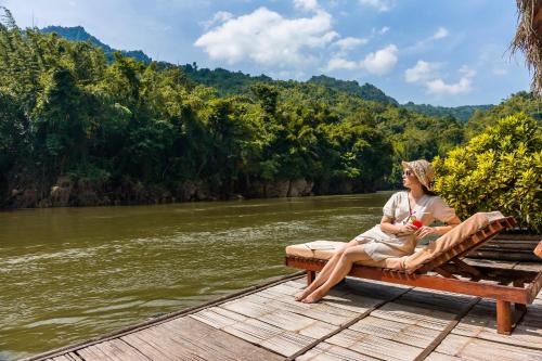 a woman sitting on a bench on a dock on a river at River Kwai Jungle Rafts in Sai Yok