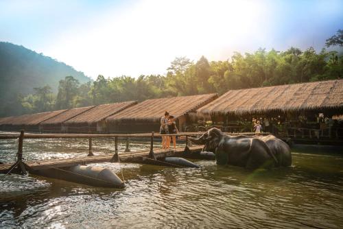 a woman standing next to an elephant in the water at River Kwai Jungle Rafts in Sai Yok