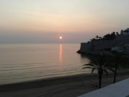 a sunset over the ocean with a palm tree on the beach at Hotel Mare Nostrum in Peñíscola