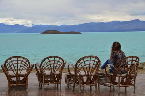 Eine Frau, die in einer Gruppe von Stühlen am Wasser sitzt. in der Unterkunft Hotel Las Dunas in El Calafate