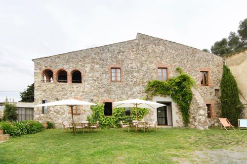 uma casa de pedra com mesas e guarda-sóis no quintal em Mas Valentí 1511 em Vall-Llobrega