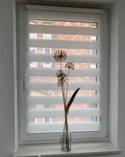 a vase with flowers in front of a window at City Apartments Hannover in Hannover