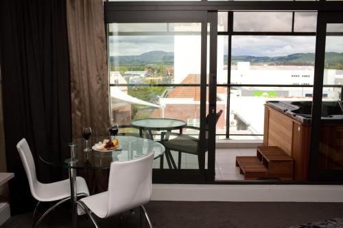 Quest Rotorua Central في روتوروا: غرفة مع طاولة زجاجية وكراسي وشرفة