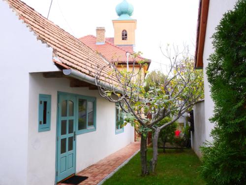 a white house with a green door and a tree at Tettyei Házikó in Pécs