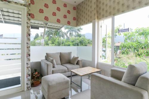 a living room with chairs and a table and windows at Griya Mulya near Alun Alun Batu Mitra RedDoorz in Batu
