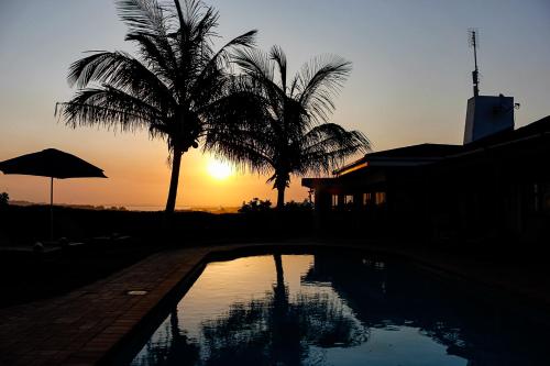 a sunset with two palm trees and a swimming pool at The Ridge Guesthouse in Richards Bay