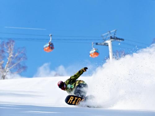 a man riding a snowboard down a snow covered slope at jyozankei Shikanoyu in Jozankei