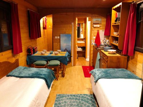 a room with two beds and a table and a kitchen at Millygite roulotte - 4 seasons Chalet-on-wheels in Milly-la-Forêt