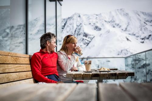 a man and woman sitting at a table in front of a mountain at DAS VIER Sport,- und Wellnesshotel in Sankt Leonhard im Pitztal