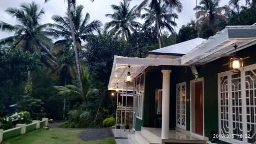 a green house with palm trees in the background at Fab Valley Homestay in Munnar