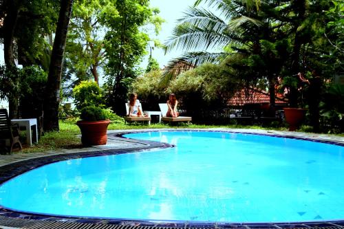 a blue swimming pool with two people sitting in a yard at Moonstone Villas in Tangalle