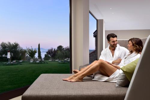 a man and woman sitting on a couch in front of a window at Borgobrufa Spa Resort Adults Only in Brufa