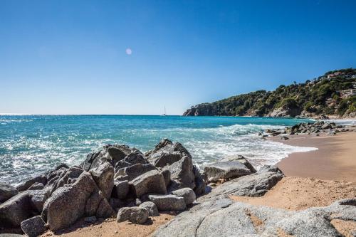 una playa con rocas y el océano en un día soleado en Camping Cala Llevado, en Tossa de Mar