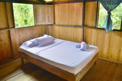 a bed in a wooden room with two windows at Posada La Sirena Negra in Nuquí