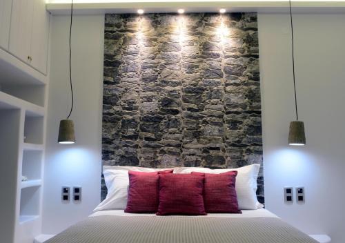 a bedroom with a stone wall and a bed with red pillows at Seashell Mandrakia Sea view in Mandrakia