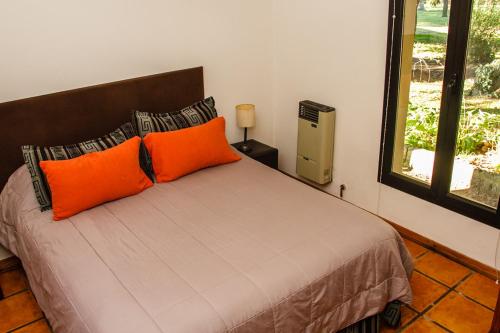 1 dormitorio con 1 cama con almohadas de color naranja y ventana en El Estanque en Tandil
