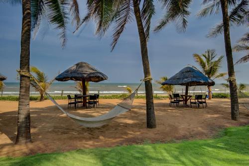 a hammock and chairs under umbrellas on a beach at Radisson Blu Resort Temple Bay Mamallapuram in Mahabalipuram