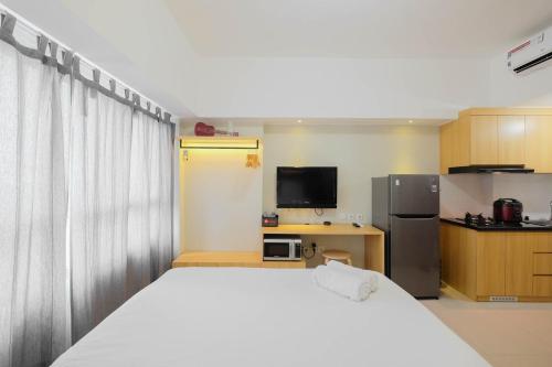 a bedroom with a white bed and a refrigerator at Modern Studio @ Springlake Summarecon Apartment By Travelio in Rawabugel