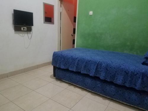 - une chambre avec un lit bleu et une télévision dans l'établissement Cendrawasih Syariah Homestay, à Lampung