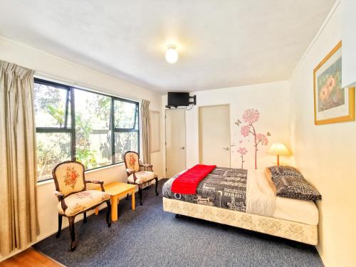 a bedroom with a bed and two chairs and a window at Atarau Grove Studio in Paraparaumu