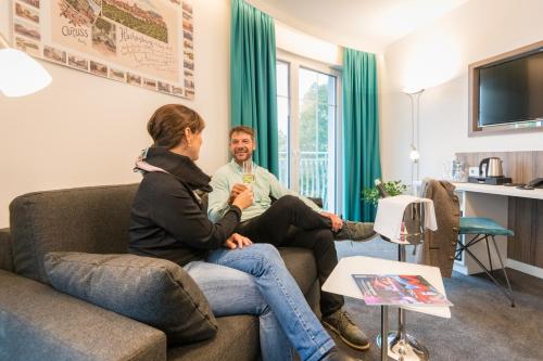 two people sitting on a couch in a living room at Parkhotel Hachenburg in Hachenburg