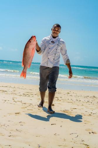 a man holding a fish on the beach at Swahili Beach in Diani Beach