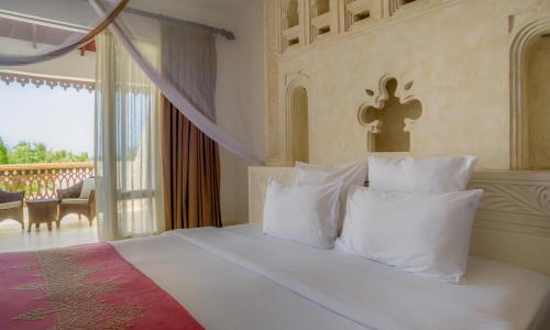 a bedroom with a bed with white pillows and a balcony at Swahili Beach in Diani Beach