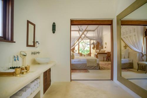 a bathroom with a mirror and a bedroom with a bed at Swahili Beach in Diani Beach