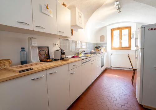 a kitchen with white cabinets and a red tile floor at Chasa Werro in Sent