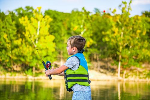 a young boy in a safety vest holding a fishing rod at Chalets Resort Luxury Lakefront Villa Amazing View 2 Pools Free Amenities Dock in Lampe