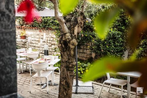 a patio with white tables and chairs and a tree at Hotel Alessandro Della Spina in Pisa