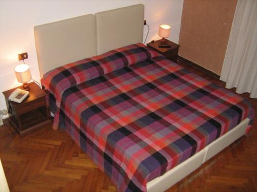 a bed with a plaid blanket and two night stands at Hotel Da Cesare in Stresa