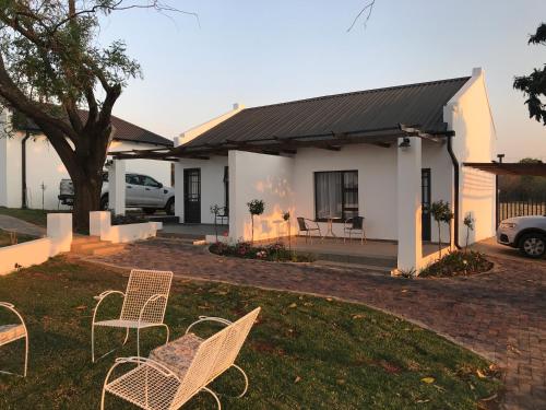 a white house with chairs in the yard at Steenkoppies Estate semi self catering unit 2 in Magaliesburg