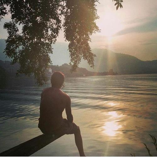 a man sitting on a bench next to a body of water at Reggae Guest House in Tuk Tuk