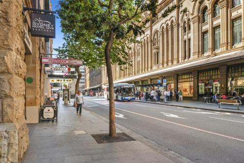 a person walking down a street with a tree on the sidewalk at YEHS Hotel Sydney QVB in Sydney
