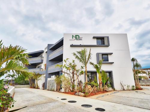 a white building with palm trees in front of it at Yomitan Condhotel ND in Yomitan