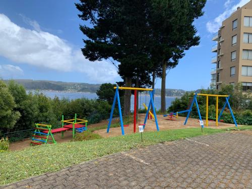 a playground with colorful swings and a tree at Departamento Esmeralda Pingueral in Dichato