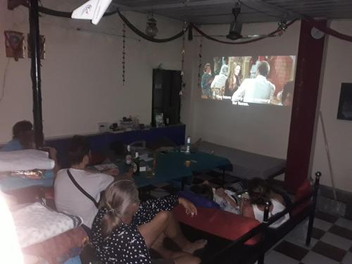 eine Gruppe von Menschen, die in einem Zimmer sitzen und einen TV schauen in der Unterkunft Black Pepper Home Stay in Udaipur