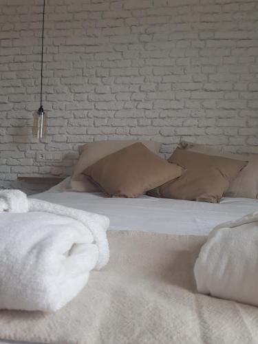 uma cama com lençóis brancos e almofadas ao lado de uma parede de tijolos em Dos Alas Rojas, casa con jacuzzi para dos personas em Mélida