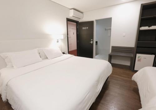 a hotel room with a large white bed and a chair at Fratele Business Hotel in Patos de Minas